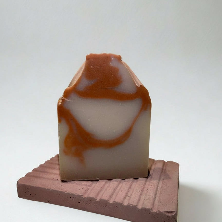 Marbled brown and beige soap bar on a wooden stand against a white background