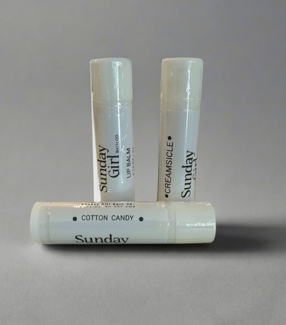 Three lip balms from Sunday Girl on a gray background